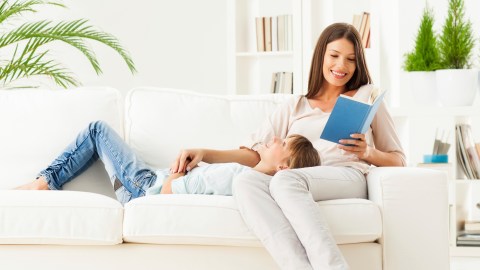 A mom reads a book about executive function to her daughter laying in her lap on the couch