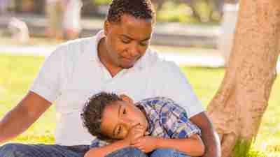 Boy with ADHD leaning on father in park outside